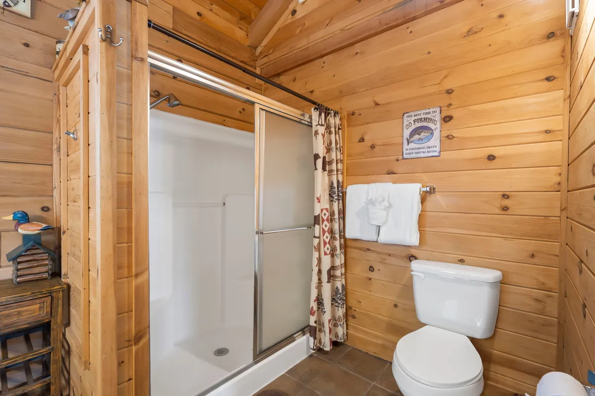 A stylish, inviting bathroom featuring a glass shower enclosure, wooden wall panels, and a wildlife-themed curtain. White towels and decorative touches complete this fresh and cozy space.