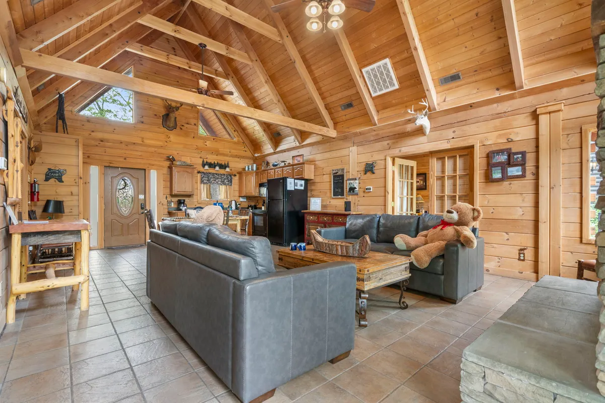 A cozy great room with a vaulted wooden ceiling, expansive windows filling the space with light, comfortable couches, and a teddy bear on the sofa. The arrangement is perfect for hosting gatherings or enjoying quiet moments together.