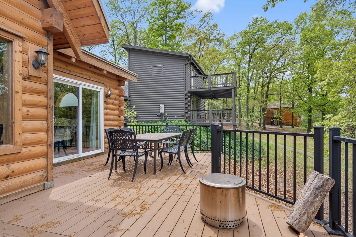 A view of a wooden deck surrounded by trees, with an outdoor dining set and fire pit. The setup highlights a social, communal space for enjoying meals or relaxing outdoors, while the natural greenery in the background enhances the sense of peaceful seclusion.