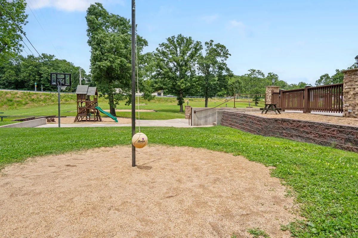 This exterior image captures a vibrant recreational area featuring a volleyball pole, children's playground, basketball hoop, and green grass. The space is clearly designed for a variety of active outdoor pursuits, with both sports facilities and family-friendly amenities visible in the same scene.