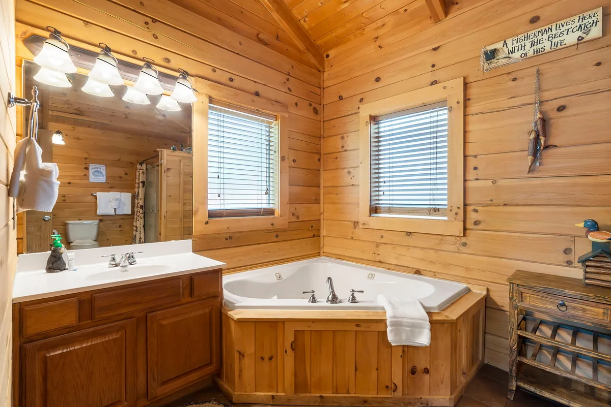 A tranquil ensuite bathroom with a deep jacuzzi tub set against wooden cabinetry, bathed in natural light from generous windows. The space exudes serenity, ideal for unwinding after outdoor activities.