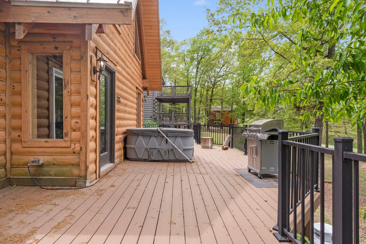 A charming wooden deck surrounded by trees, featuring a bubbling hot tub and a grill. The secluded atmosphere is perfect for unwinding after a day of exploring, with opportunities for both relaxation in the hot tub and shared outdoor meals. The setting hints at privacy, comfort, and a seamless connection with nature.