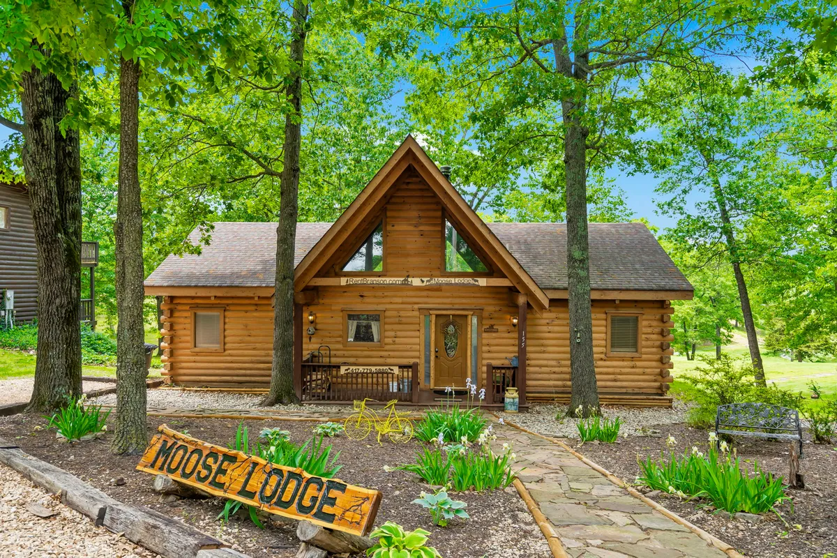 This image displays the front of Moose Lodge, with its cozy log cabin architecture, a prominent Moose Lodge sign, inviting front porch seating, and the backdrop of surrounding trees. It evokes a feeling of arrival and welcome, suggesting a peaceful and accessible retreat.